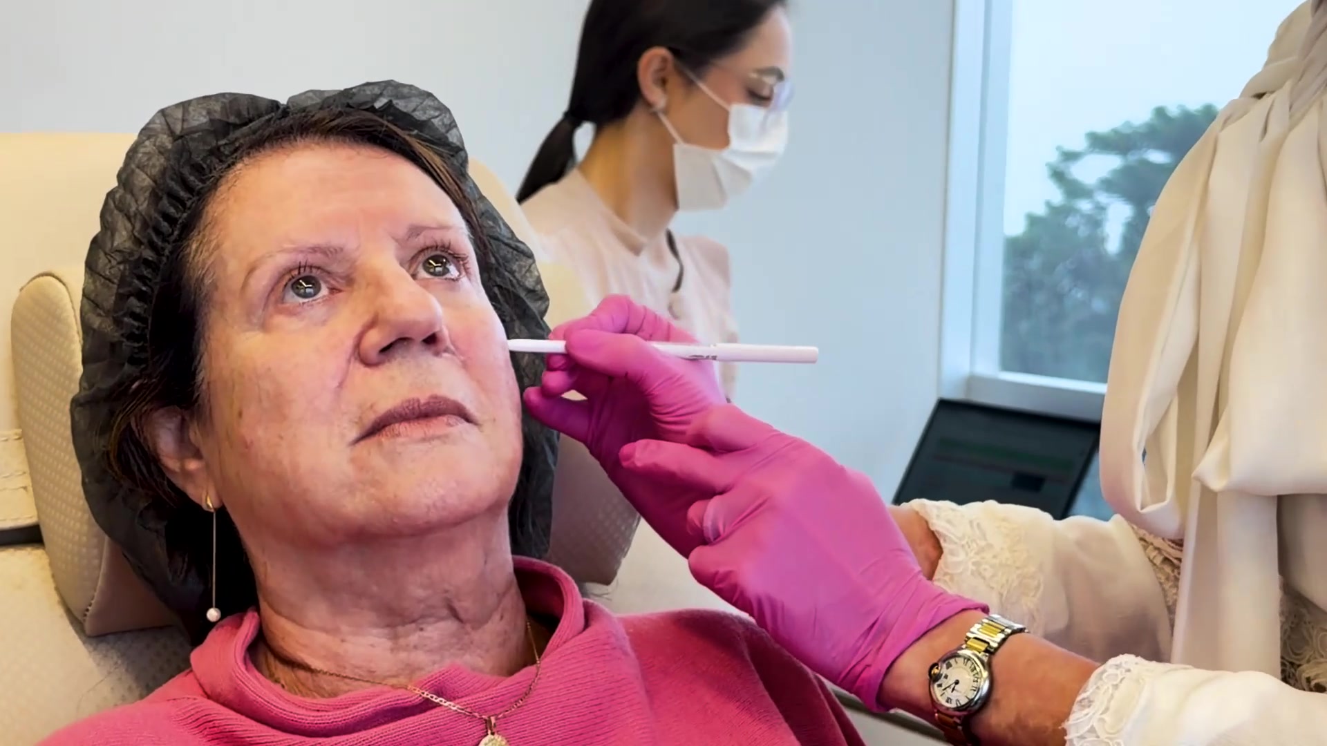 Médica avalia a face da paciente sentada, lápis demarcador em mãos, antes de qualquer marcação